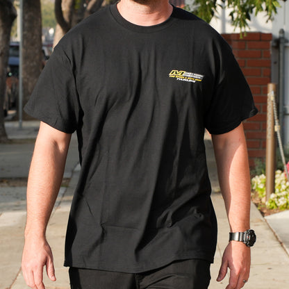 Person wearing a black t-shirt with a logo on the chest, standing outdoors.